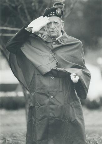 An older man in a uniform and long coat, wearing white gloves and a beret or tam, salutes while…