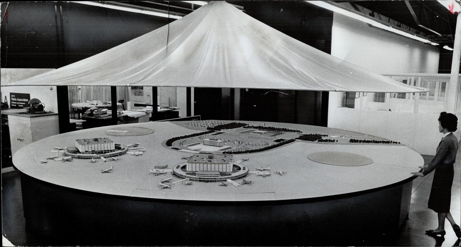 Mrs. M. Kwan studies model of Toronto's new international airport which goes into operation Jan 12, Circular building at left is second aeroquay plann(...)