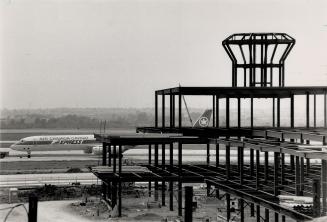 The skeleton of the new ground control tower rises above the aircraft parking apron, right