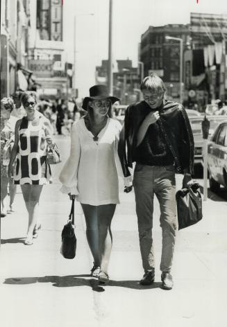 Mr. And Mrs. Michael Cooper Strolling Along. She wears white mini and floppy hat, he wears sweater an corduroy pants