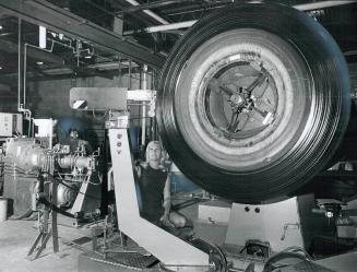 Mighty Tire Machine, Big tire retreading machine, dwarfing typist Linda Young at United Tire works at Rexdale, is said to be the only one of its kind (...)