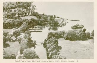 A steam ferry approaches the island harbour. In the foreground, a small bridge spans thee river…