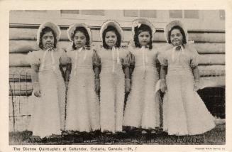 Black and white photograph of four identical little girls in long dresses and bonnets.