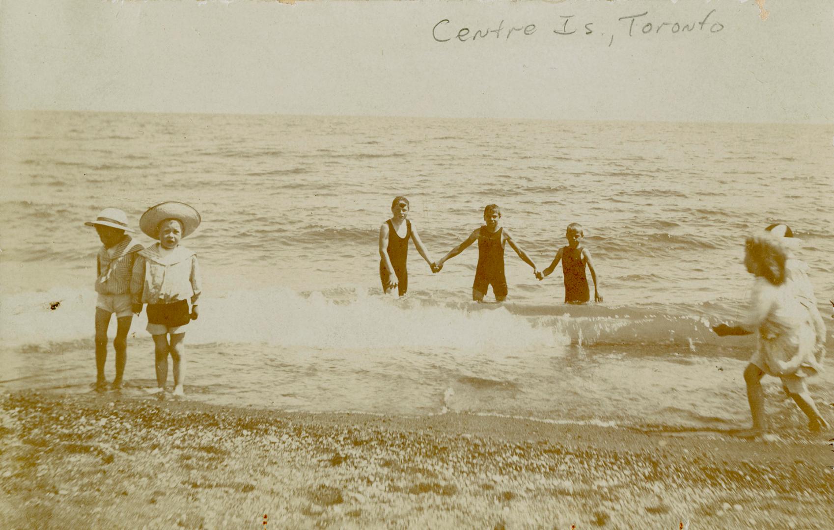 Sepia toned picture of 6 children paddling in a lake.