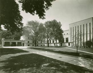 View of library building and three car garage with lawns and driveway and trees in foreground. 