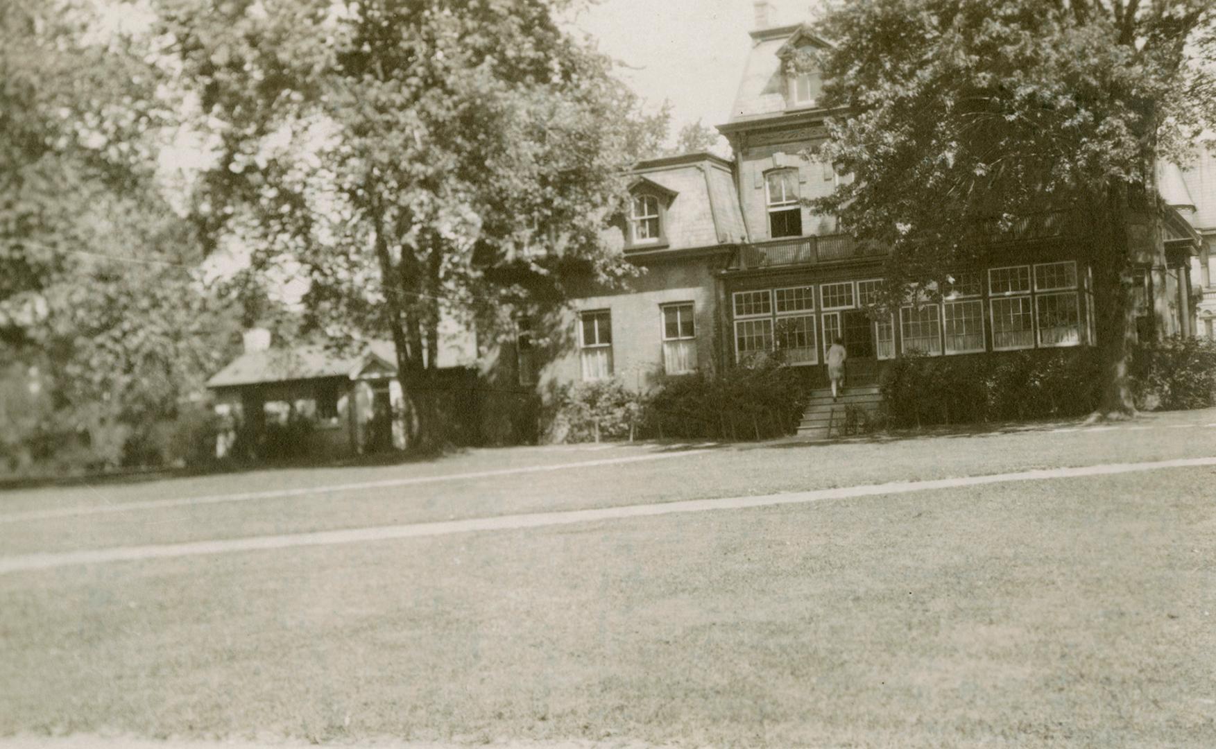 Photo taken from some distance with large lawn in front and large Victorian House surrounded by ...