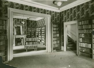 Photo of interior view of room with bookshelves lining the walls and patterned wallpaper on the ...