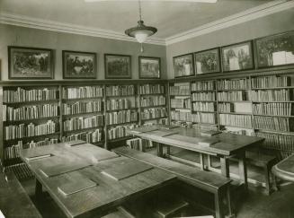 A room in Boys and Girls House lined with walls lined with books and two large wooden tables wi ...