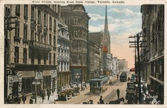 Colorized photograph of a busy city street with tall buildings, cars, people and streetcars.
