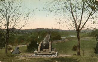 Colorized photograph of a man sitting down beside a cannon overlooking a valley with a river in ...