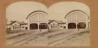 Pictures show a covered barn for trains along side a one-story public building.