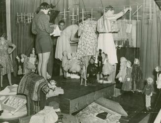 Picture of a group of people standing on a stage setting up puppets for a puppet show. 