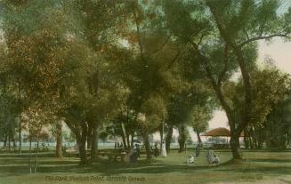 Picture of a few people in a shaded picnic area of a park with large trees.