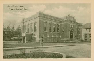 Picture of street scene with large public library with man standing outside and houses to the r ...