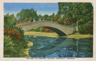 Bridge over water with four people on the bridge surrounded by trees and shrubs. 
