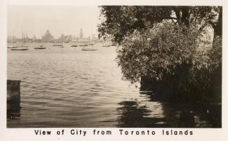 Black and white photograph of the shoreline of an island with sailboats and a cityscape in the  ...