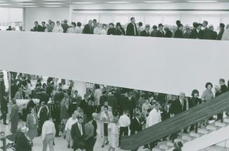 Picture of crowds of people on the first floor, stairs and balcony of a library. 