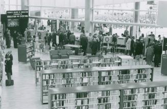 Picture of crowds of people in a library looking at displays and books on shelves.