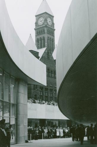 Picture of outside of modern City Hall with tower of old building in background. 