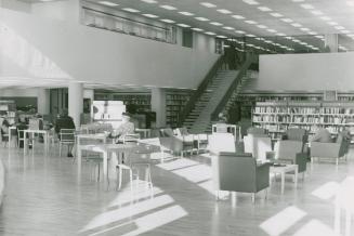 Picture of chairs and tables in a sun lite library with staircase to balcony in background. 