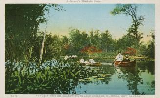 Many people in canoes on a lake in a wooded area.