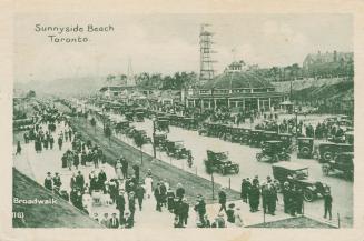 Picture of an amusement park with a road crowded with cars and people walking on a boardwalk. 