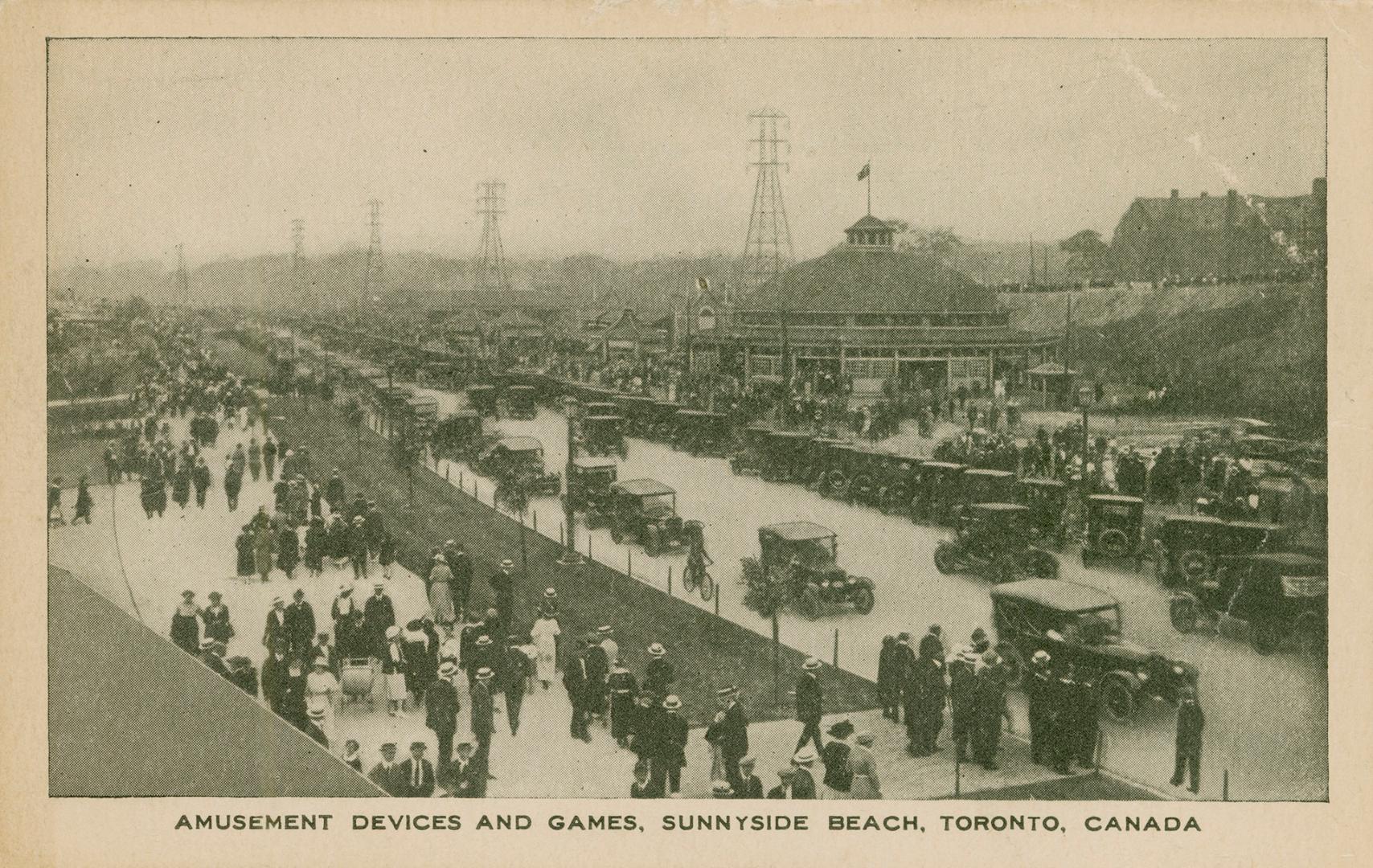 Picture of an amusement park with a road crowded with cars and people walking on a boardwalk. 