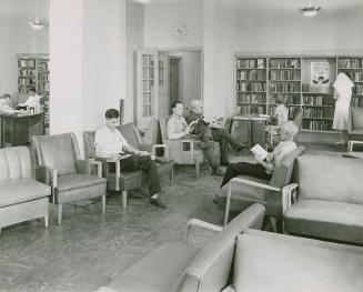 A group of men sit in chairs reading in a library. 