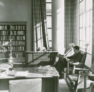 Picture of two people sitting reading in a library. 