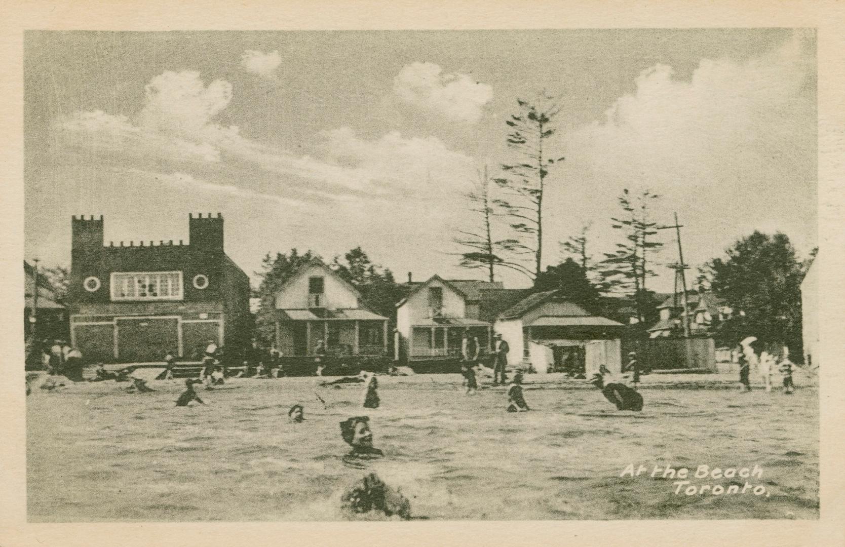 Black and white picture of people swimming in water with arcade buildings on the shoreline.