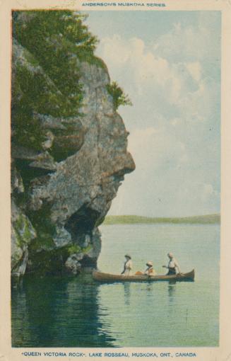 Three women in a canoe beside a rock formation that resembles a giant head.