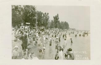 Black and white picture of a crowd of people splashing the water beside a sandy beach.