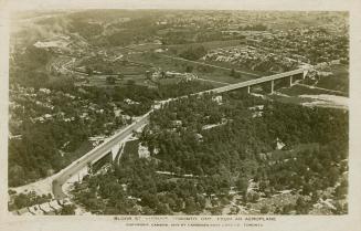 Aerial shot of a raised roadway running over a wooded area in a city. Black and white.