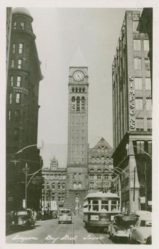 Black and white photograph of a busy city street with a large public building with a clock towe ...