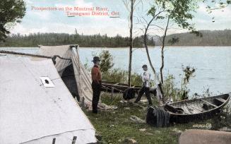 Colorized photograph of two men in their bush camp beside a lake.
