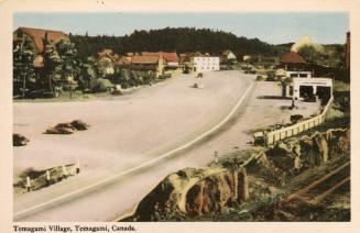 Colorized photograph of a highway going through a small town in the wilderness.