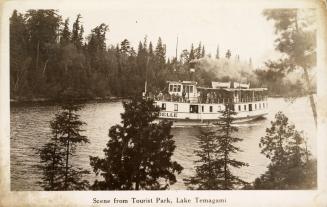 Black and white photograph of a lake in the wilderness with a steamboat cruising on it.