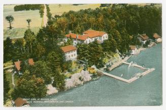 Colorized photograph of a resort beside a lake, taken from the air.