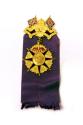 A metal pin attached to a purple ribbon. The medal shows the profiles of the Duke and Duchess o ...