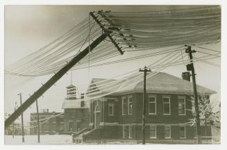 Picture of ice storm and leaning hydro pole covered in ice with library in background. 
