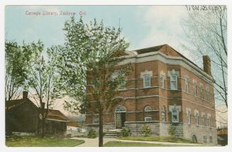 Picture of two storey brick library building with trees out front. 