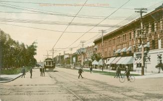 Picture of a wide street with buildings on one side, trees on other. Streetcar coming down the  ...