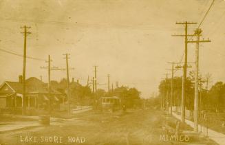 Black and white photograph of a streetcar running along a road in front of cottages.