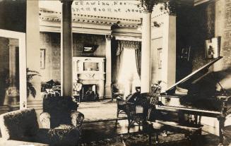 Black and white photograph of the the interior of a lavish living room with a grand piano.