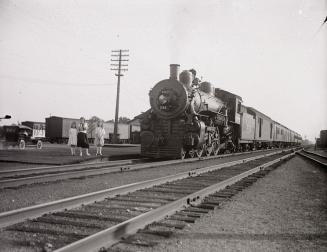 A photograph of a rail yard, with a stationary train pointed towards the photographer on one se ...