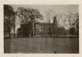 A photograph of a large three-story building with towers located at the front two corners. The …