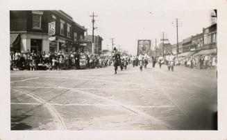 A photograph of a parade in the middle of a paved city street, with many spectators lining the  ...