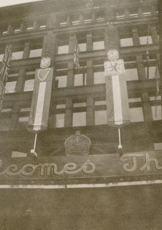 A photograph of a five story brick building decorated with bunting, a crown display and Royal c ...