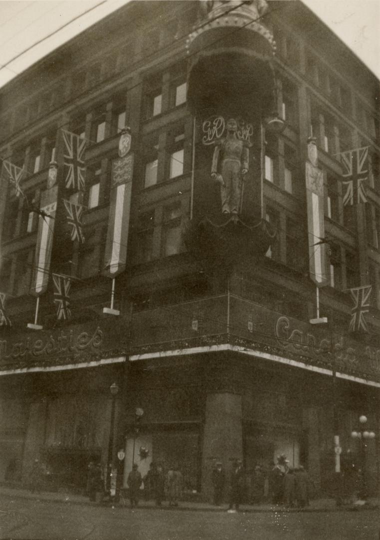 A photograph of a five story brick building decorated with bunting, a large crown sculpture and ...