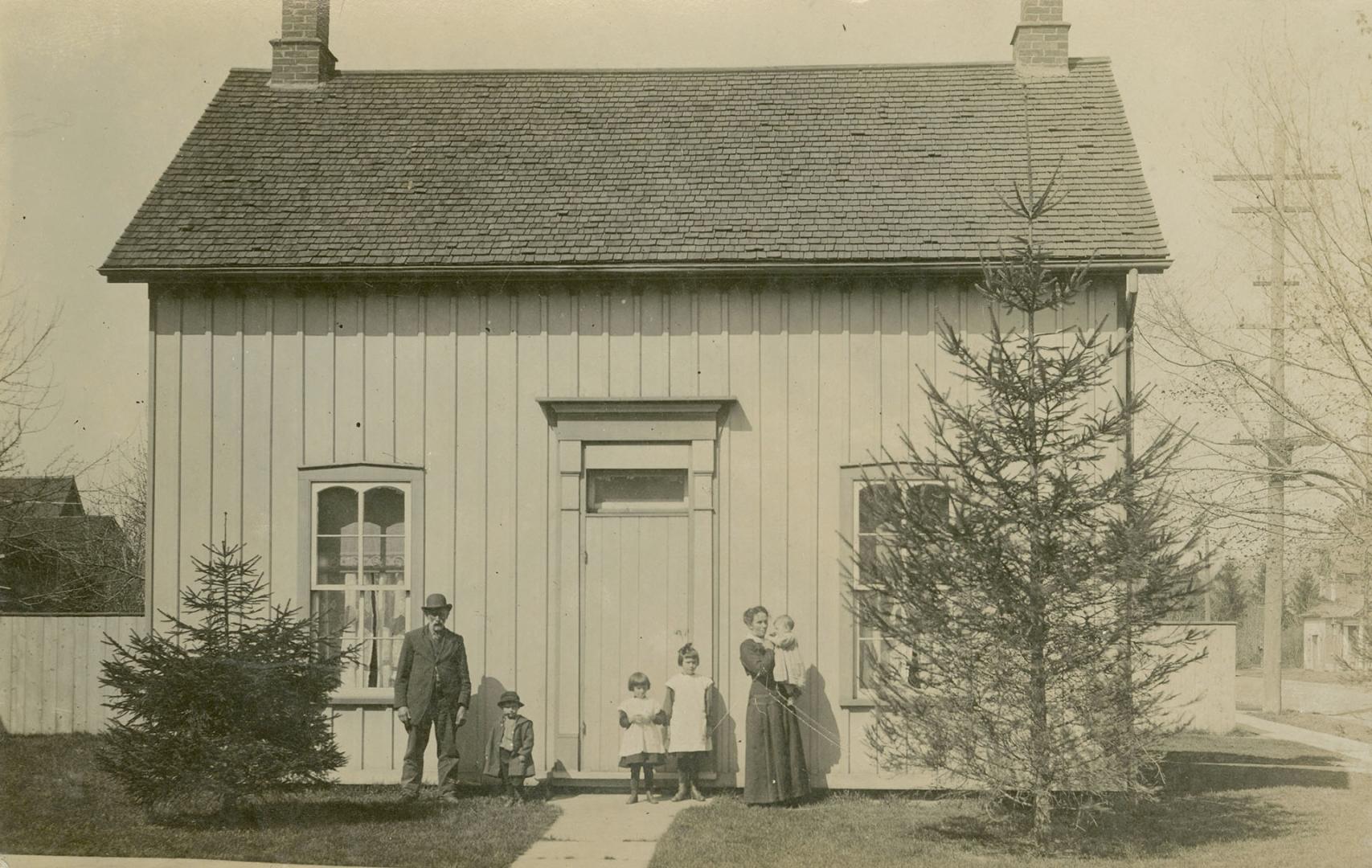 Black and white photograph of a man and a woman with four young children standing in front of a ...